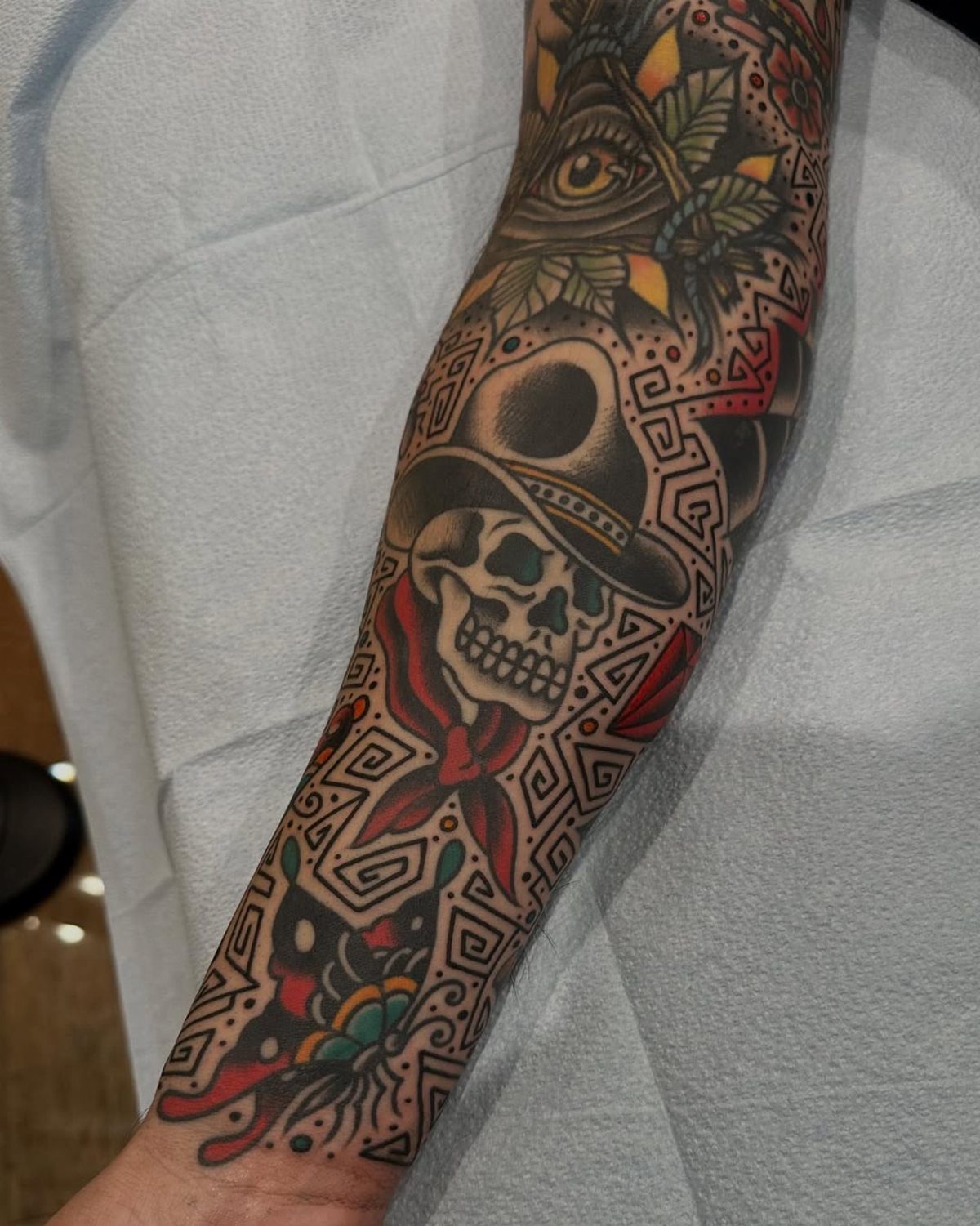 A forearm featuring various American traditional style tattoos including a skull and geometric patterns.