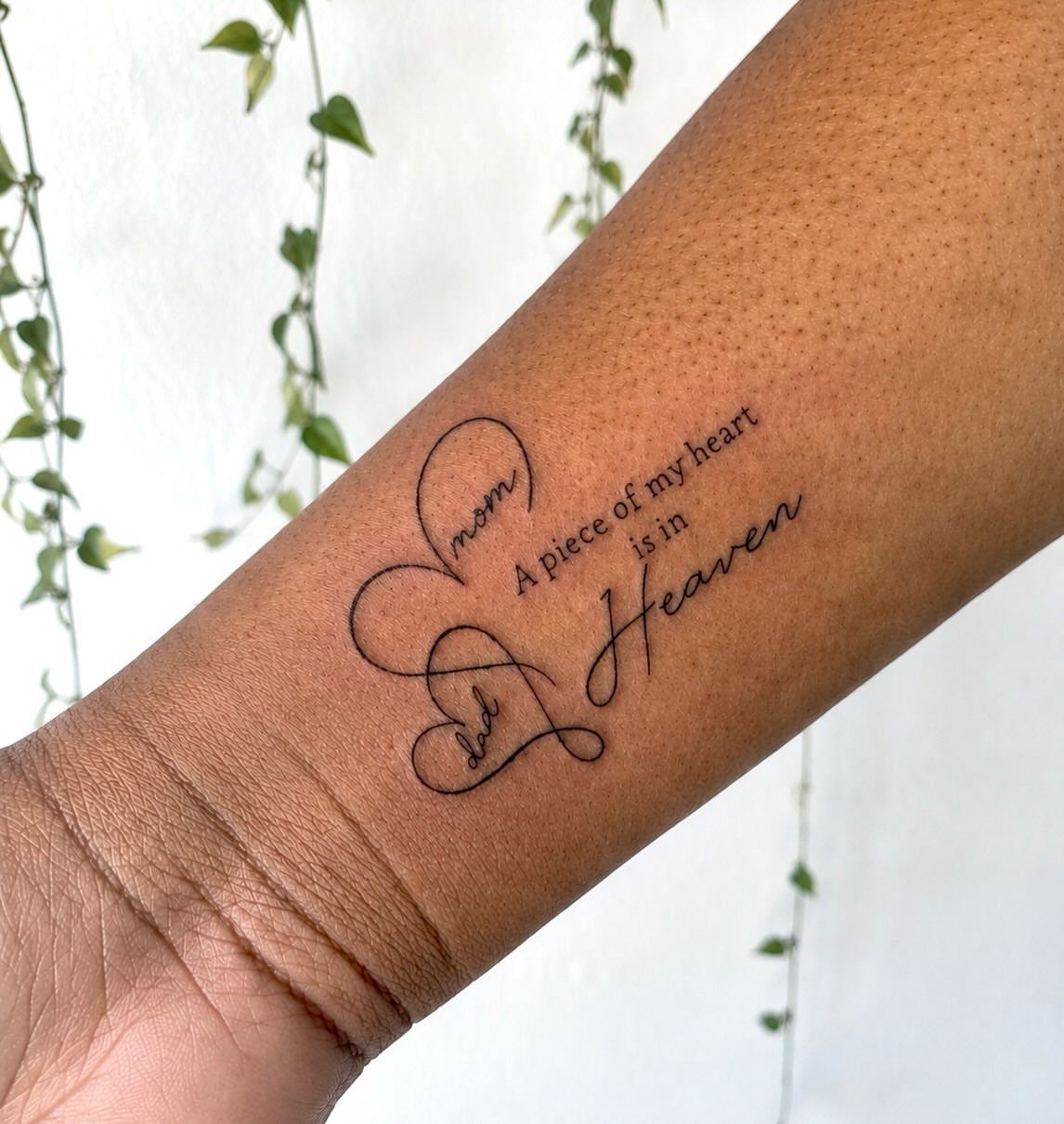 A fine-line black ink tattoo on a forearm featuring a heart made of words.