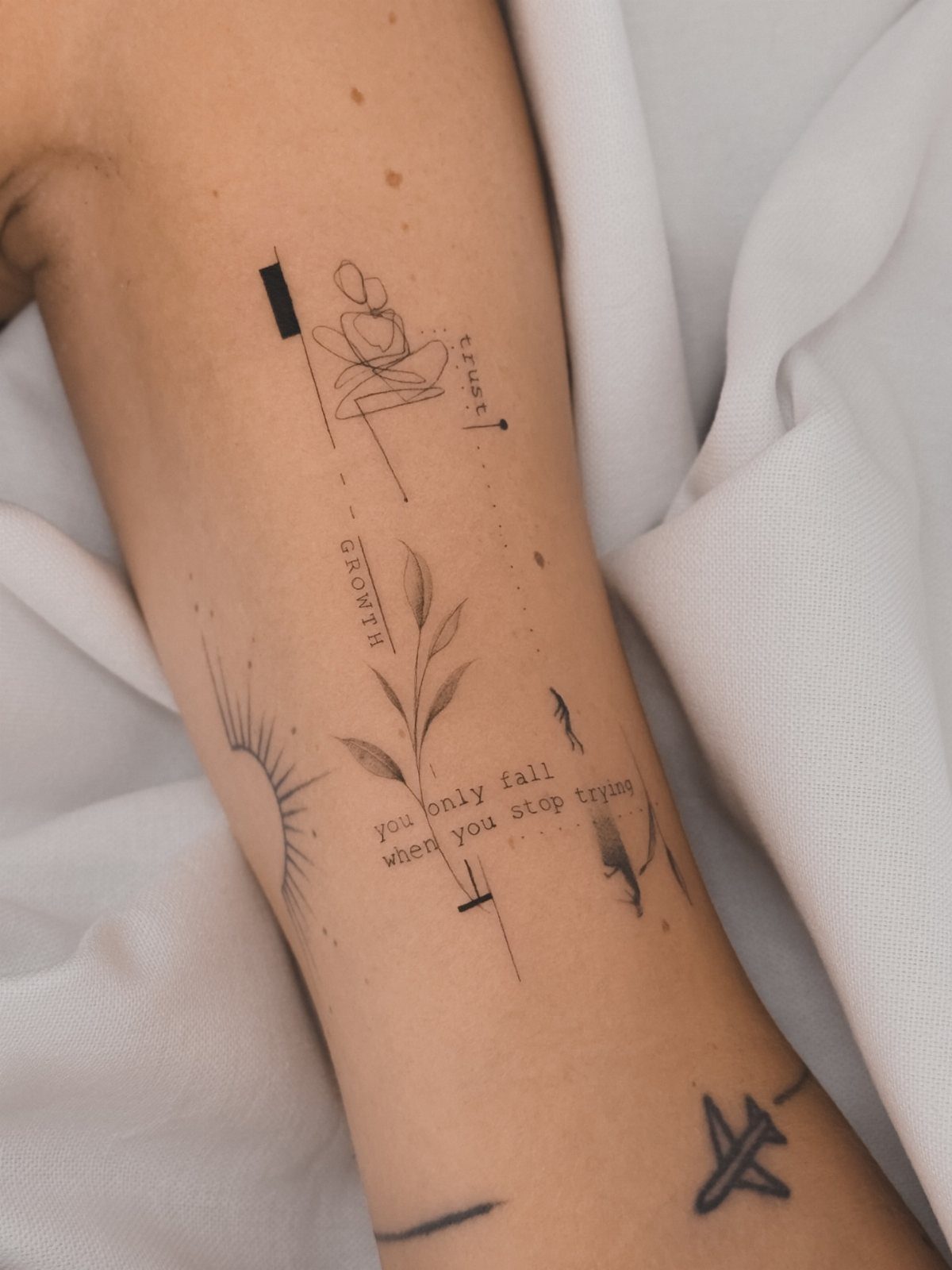 A person's arm decorated with various minimalist fine line black ink tattoos.