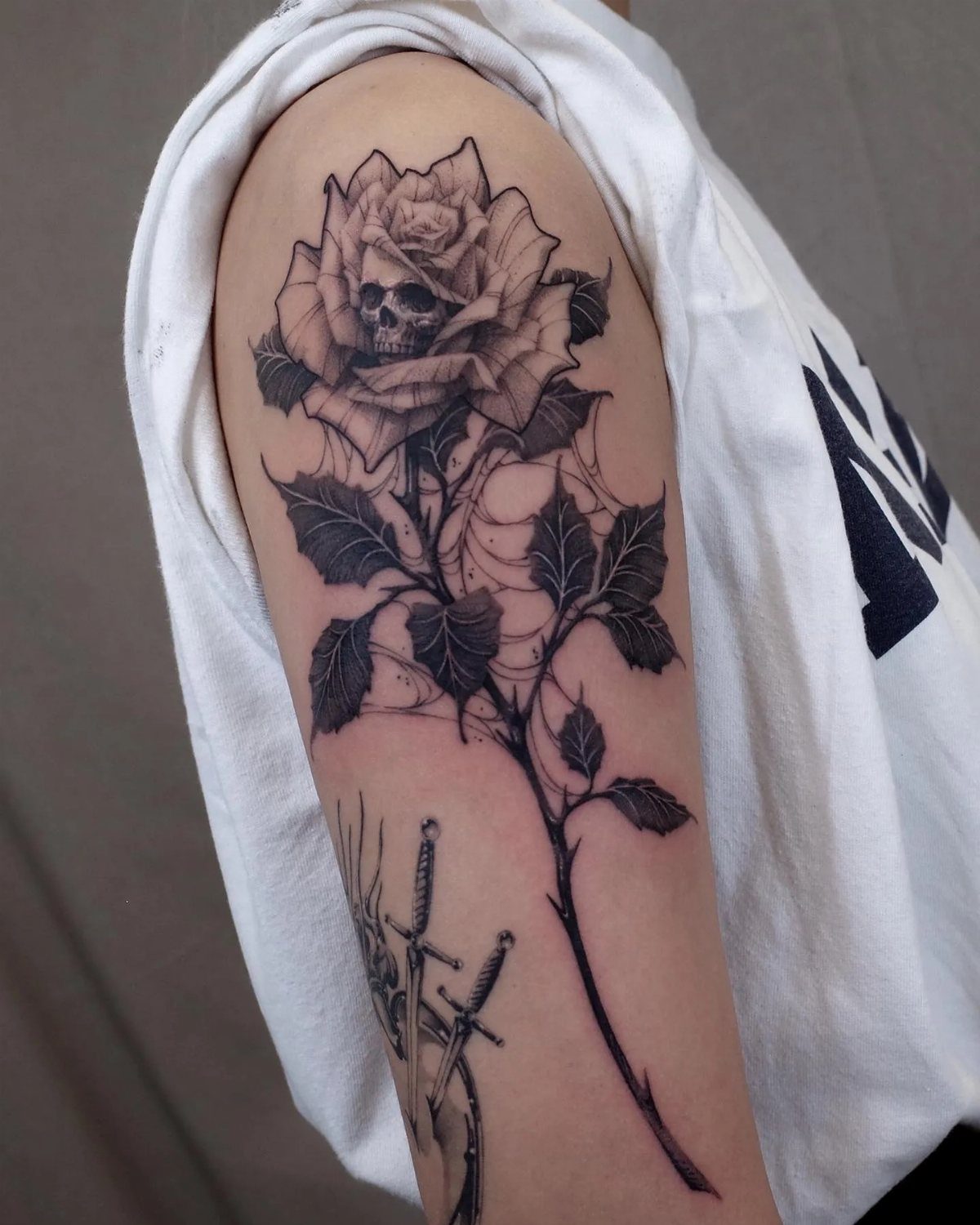 A black ink tattoo of a rose with a small skull in the center on an arm.