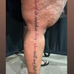 A vertical script tattoo on a person's leg reading God is within her she will not fail.
