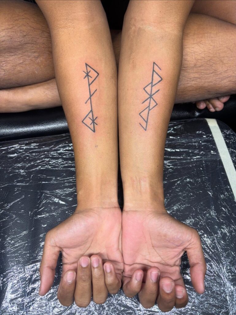 Two forearms side by side displaying black ink Nordic rune tattoos on tan skin.