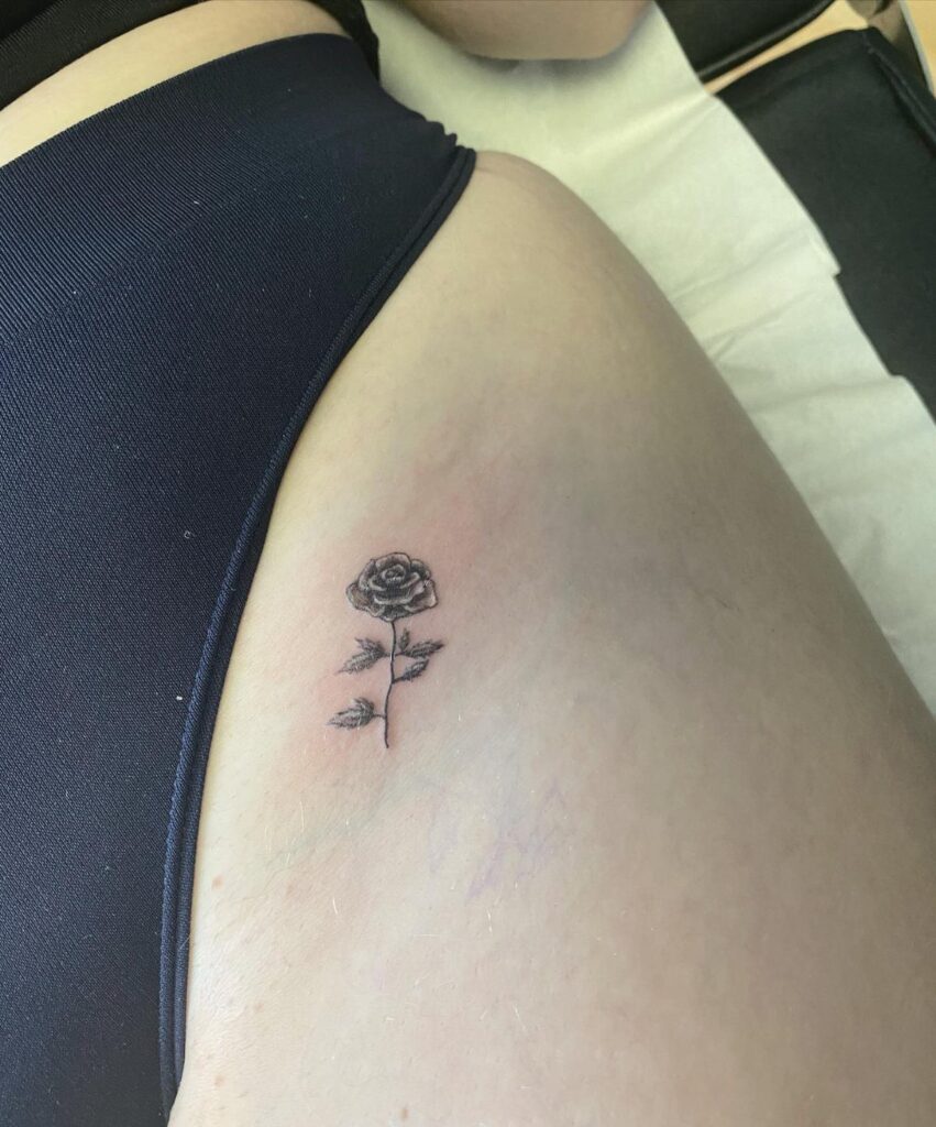 A small black rose tattoo with leaves on a person's hip skin.
