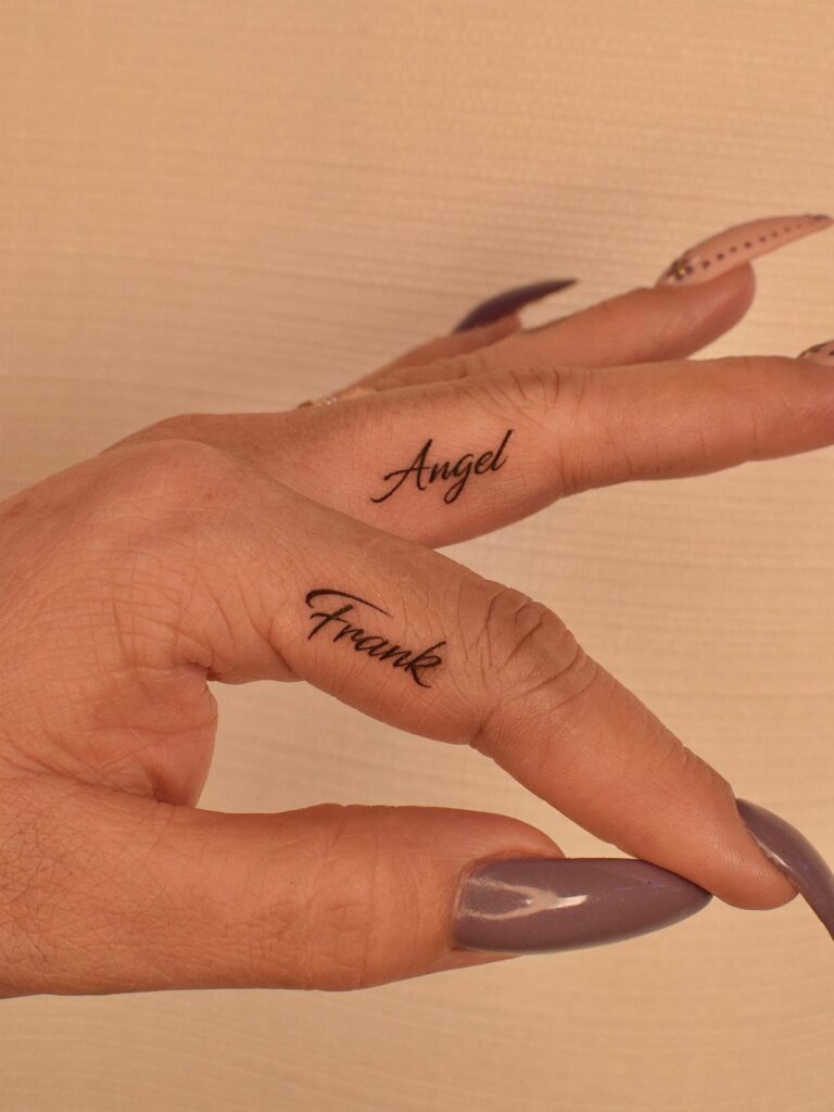 Two fingers with cursive script tattoos reading Angel and Frank against a beige background.