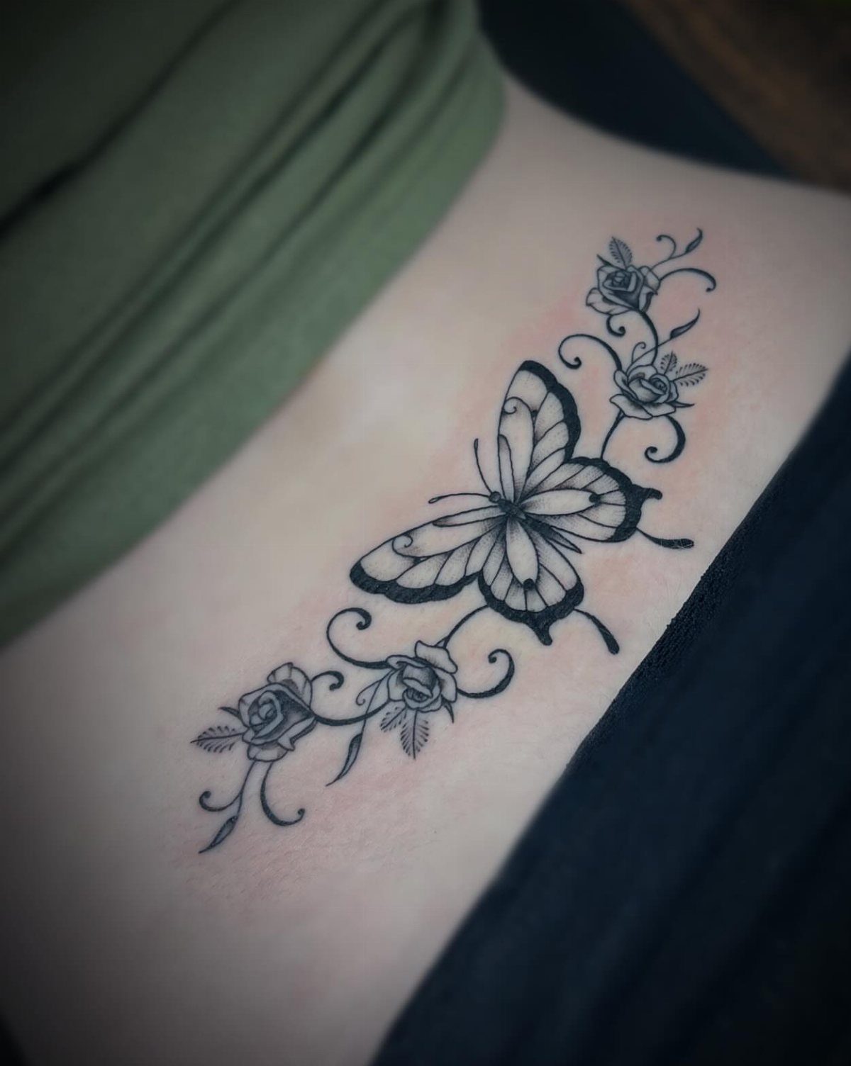 A black ink butterfly and rose tattoo design on a person's skin.