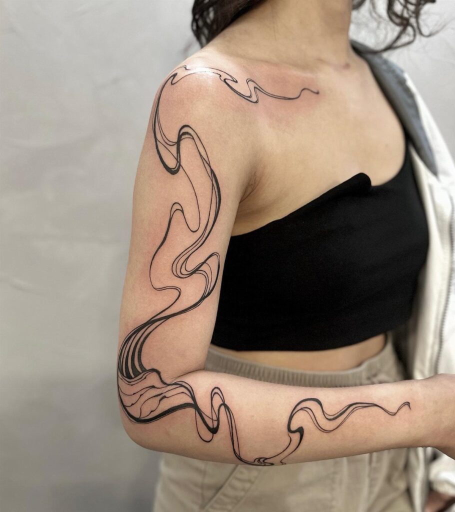 A person's arm displaying a large, flowing black line art tattoo wrapping around the shoulder.