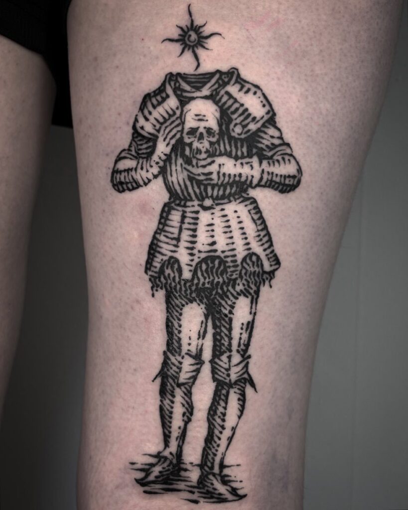 A woodcut style black ink tattoo of a headless suit of armor holding a skull on a leg.