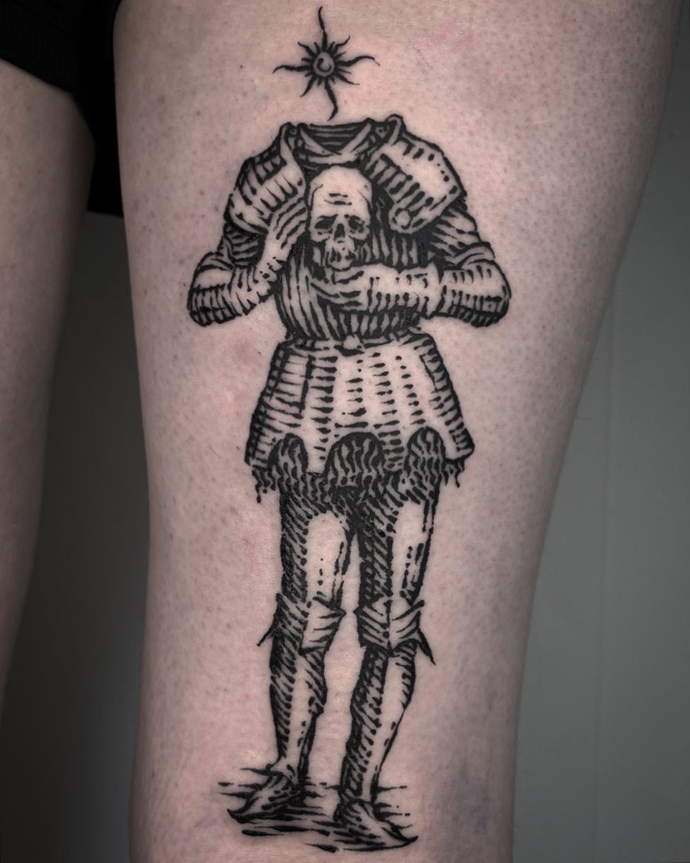 A woodcut style black ink tattoo of a headless suit of armor holding a skull on a leg.