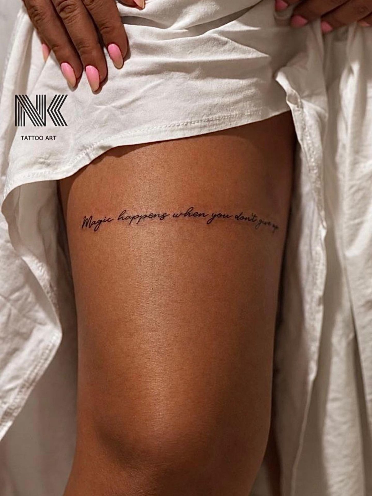 A script tattoo reading 'Magic happens when you don't give up' on a person's thigh.