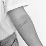 A small tattoo of geographic coordinates on a person's forearm in black and white.