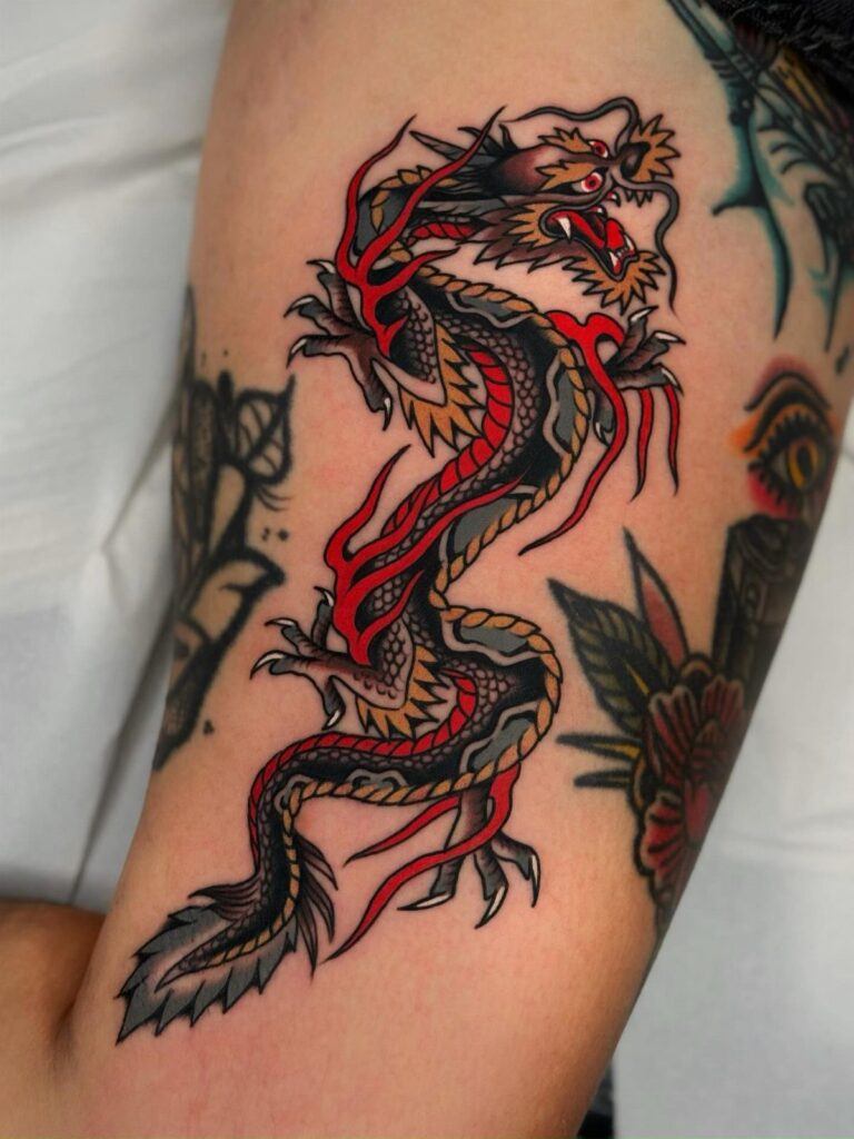 A traditional style dragon tattoo with red and gold scales on a person's arm.