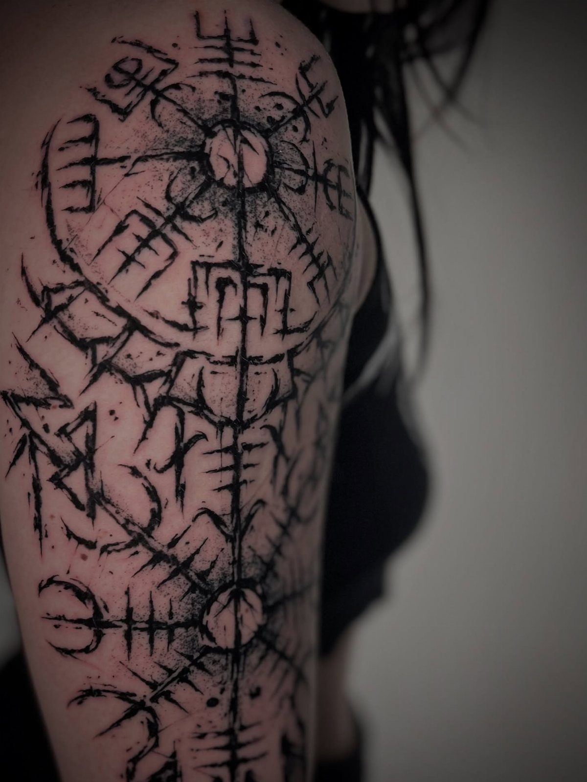 A large black ink Viking rune tattoo covering a person's shoulder and upper arm.