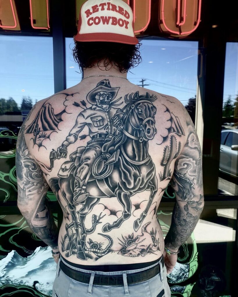 A man's back featuring a large black and grey cowboy riding a horse tattoo.